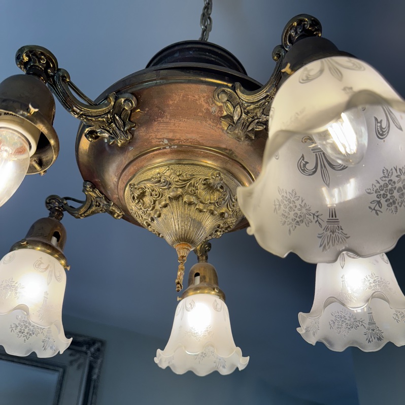 Ornate brass chandelier from early 20th century with etched glass shades.